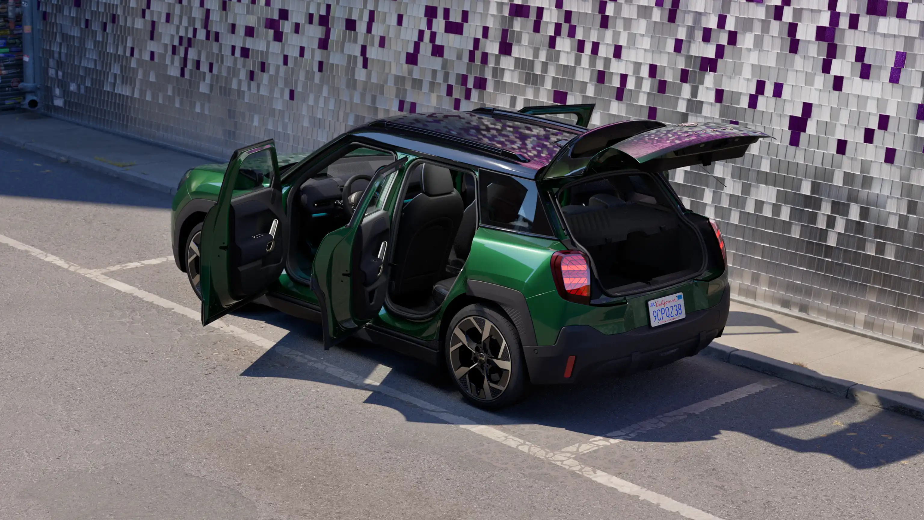 Pohled z boku na elektrické MINI Aceman v zelené barvě British Racing Green na parkovišti s otevřenými dveřmi a barevnou stěnou v pozadí