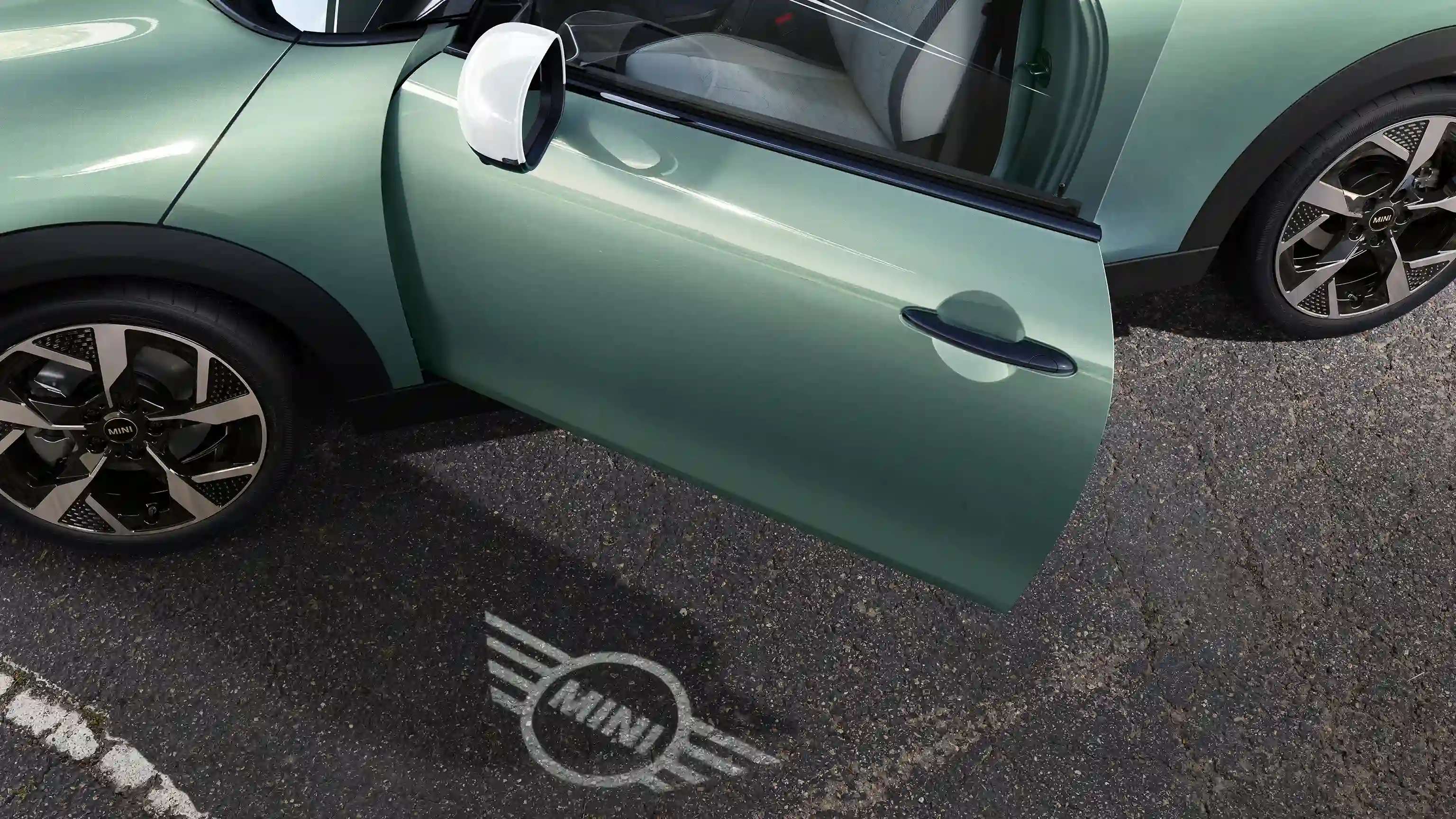Pohled zvenku na MINI Cooper s otevřenými dveřmi a uvítacím světlem s logem MINI na zemi