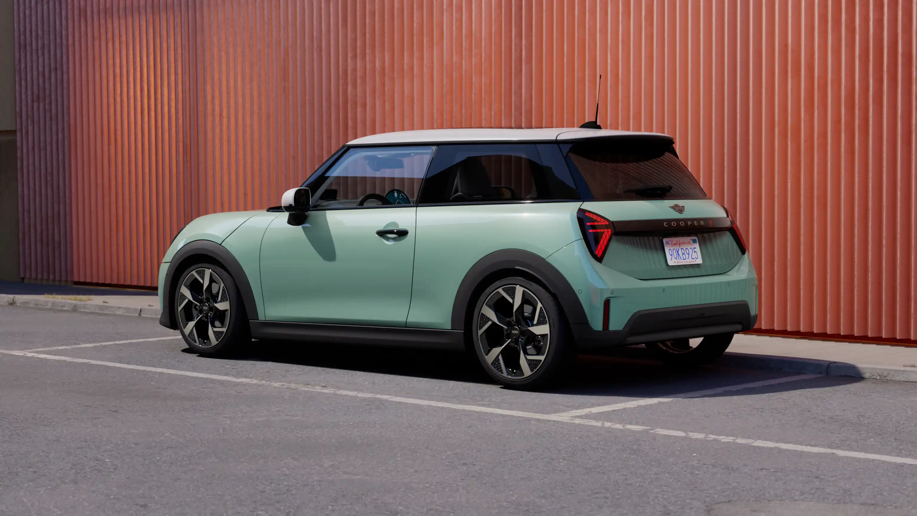 Pohled zezadu zleva na parkující MINI Cooper v zelené barvě Ocean Wave Green s bílou střechou