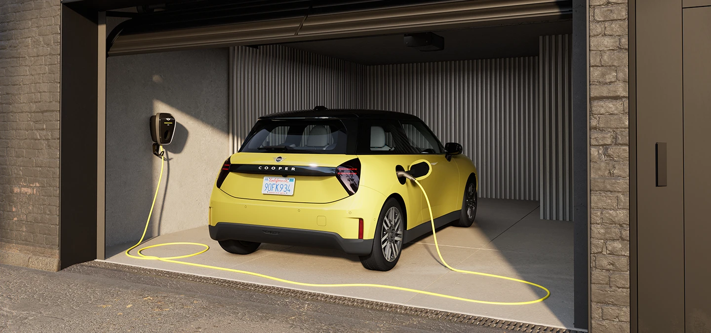 Pohled zezadu na elektrické MINI Cooper ve žluté barvě Sunnyside Yellow při nabíjení v garáži. 