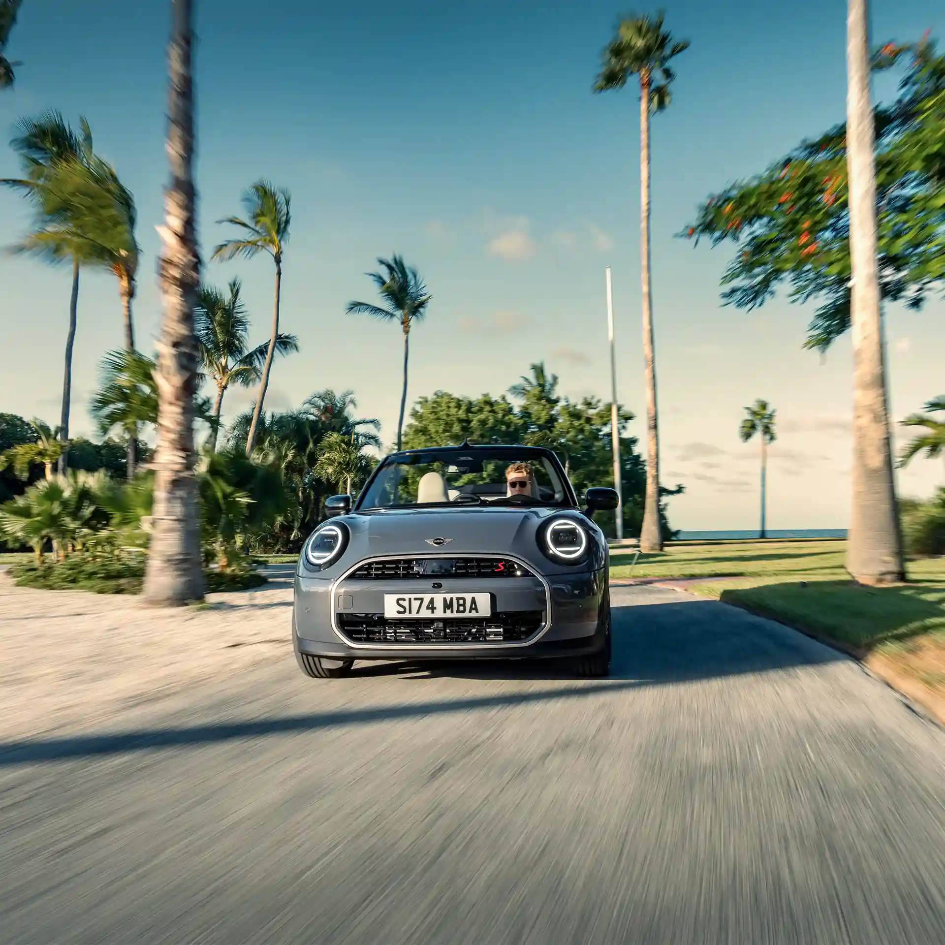 Pohled zepředu na MINI Cooper Cabrio v šedé barvě Copper Grey jedoucí po ulici