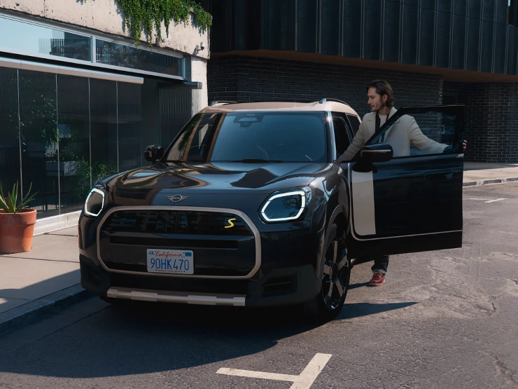 Pohled zepředu na elektrické MINI Countryman v černé barvě Midnight Black se stříbrnou střechou Vibrant Silver na ulici.