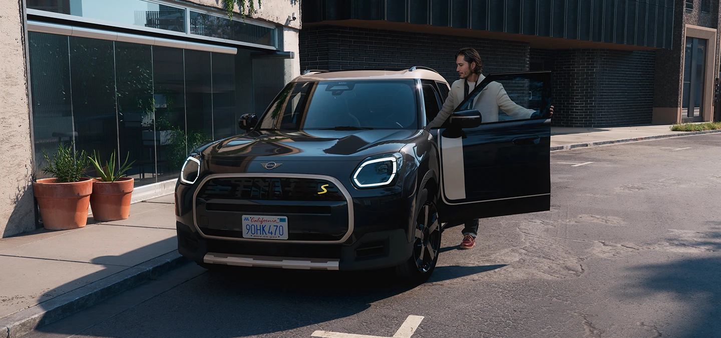 Pohled zepředu na elektrické MINI Countryman v černé barvě Midnight Black se stříbrnou střechou Vibrant Silver na ulici.