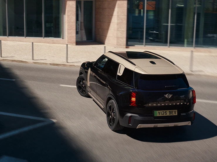 Pohled zezadu shora na zaparkované elektrické MINI Countryman v černé barvě Midnight Black se stříbrnou střechou Vibrant Silver.