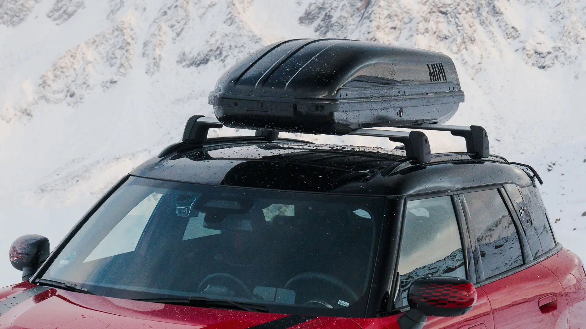 MINI Countryman v červené barvě Chili Red II s MINI Střešním boxem 320 v černé barvě.