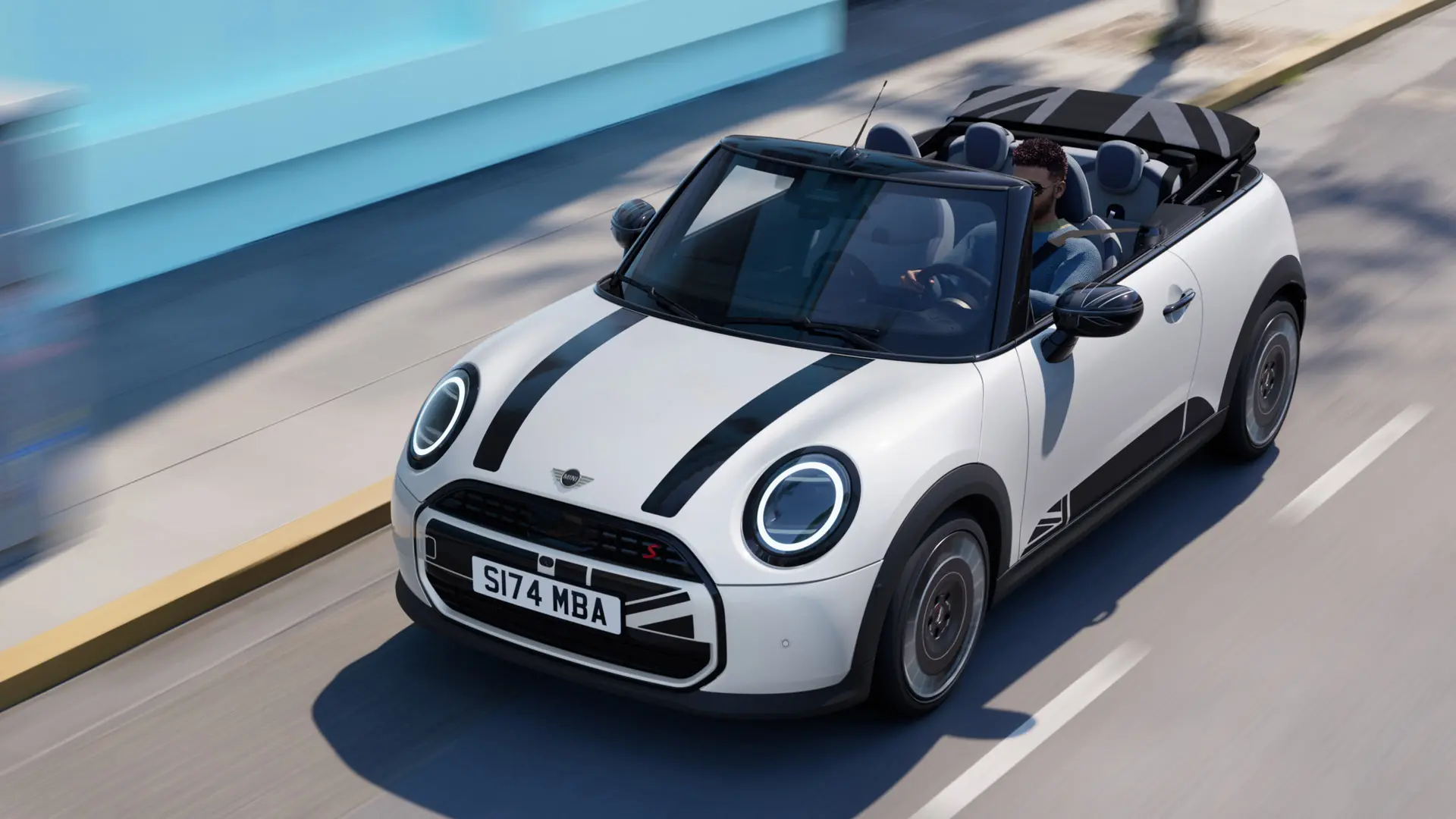 Pohled shora na MINI Cabrio v bílé barvě Nanuq White s polepy MINI Heritage na kapotě v černé barvě. 