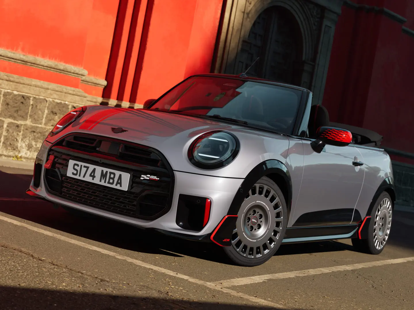 MINI Cabrio ve stříbrné barvě se sportovními doplňky JCW, včetně krytů zrcátek MINI JCW, sportovních pruhů a wingletů.
