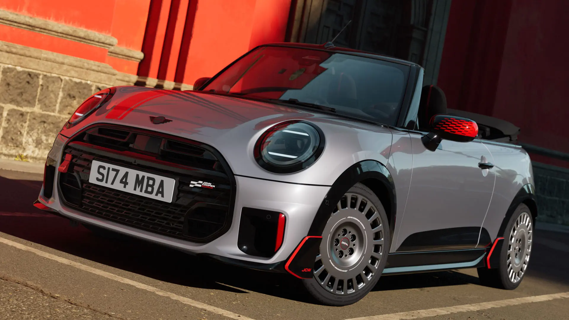 MINI Cabrio ve stříbrné barvě se sportovními doplňky JCW, včetně krytů zrcátek MINI JCW, sportovních pruhů a wingletů.