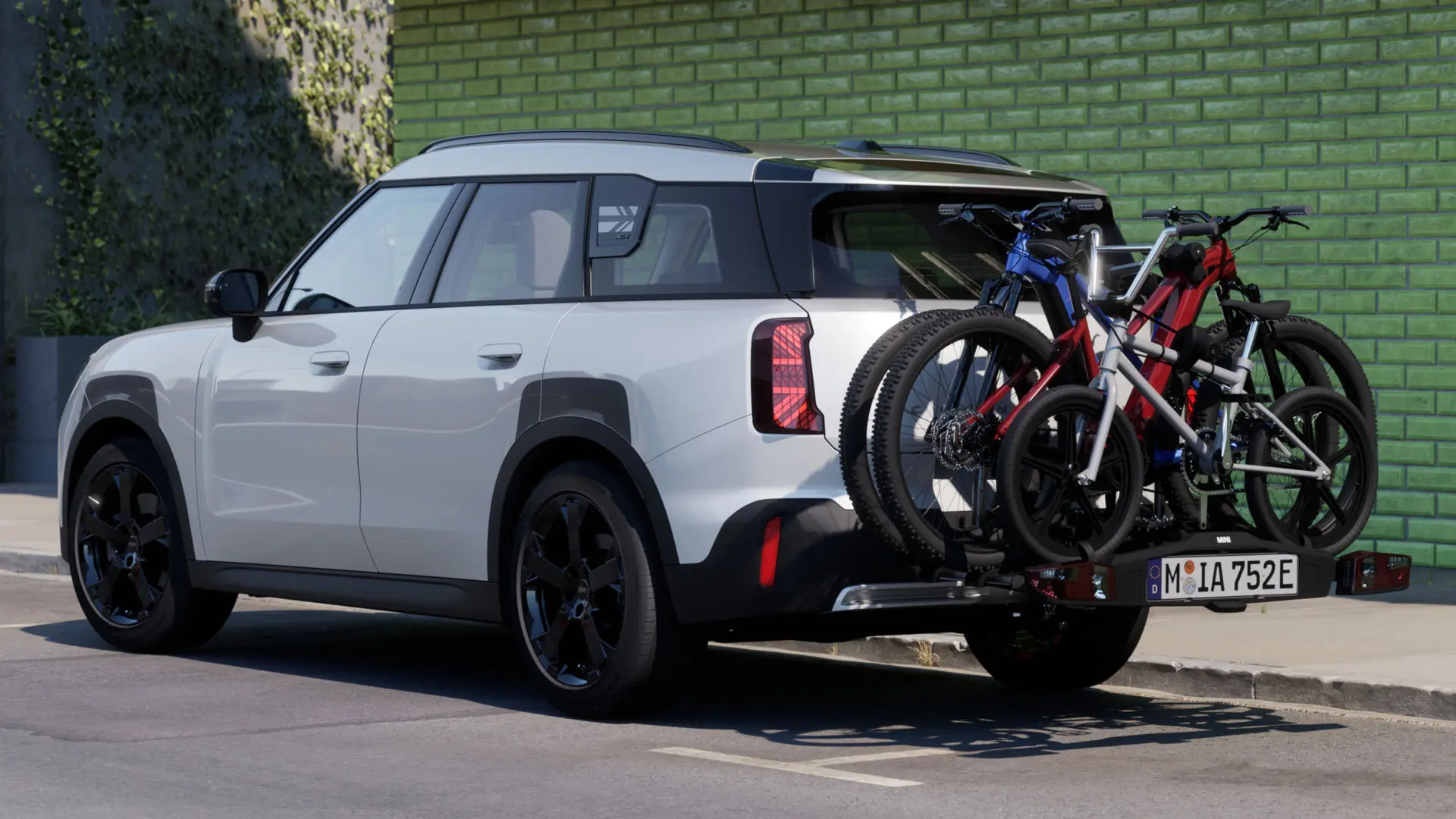 MINI Aceman v bílé barvě Nanuq White vybavené MINI Zadním nosičem kol Pro 3.0, na kterém se přepravují dvě horská kola a dětské kolo.