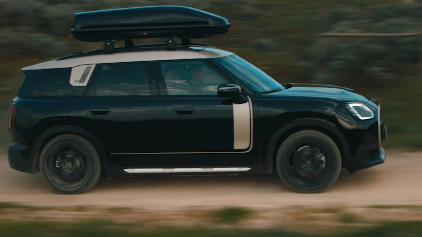 MINI Countryman s metalickým černým lakem Midnight Black s 19" John Cooper Works koly Runway Spoke v černé barvě jedoucí v terénu. 