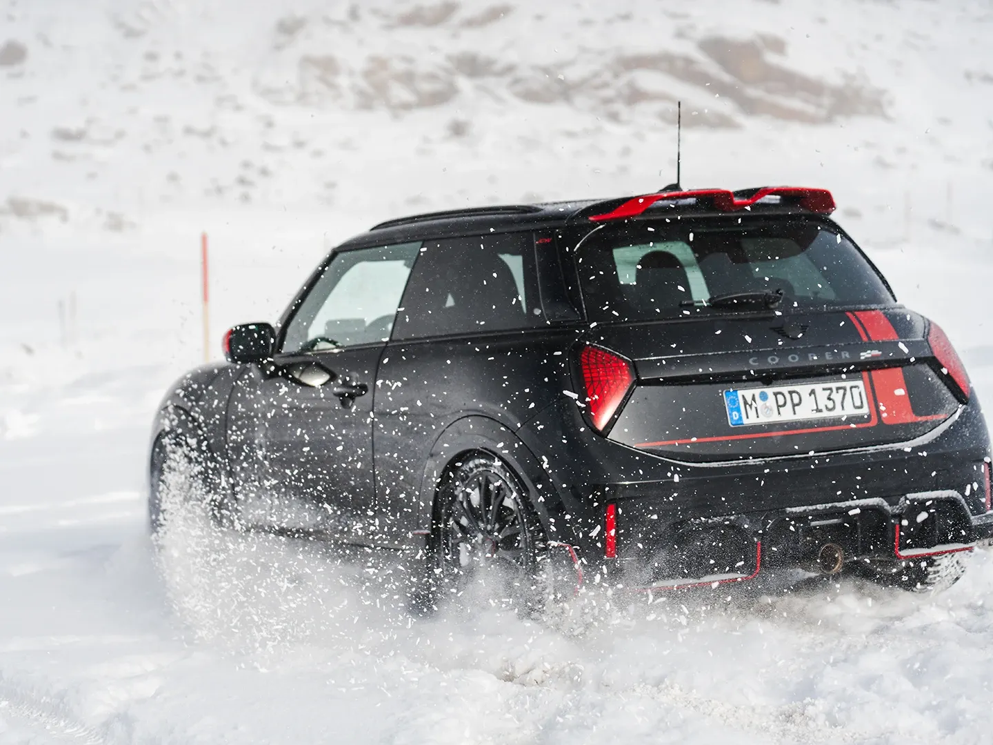 Pohled zezadu na MINI Cooper JCW jedoucí po sněhu.