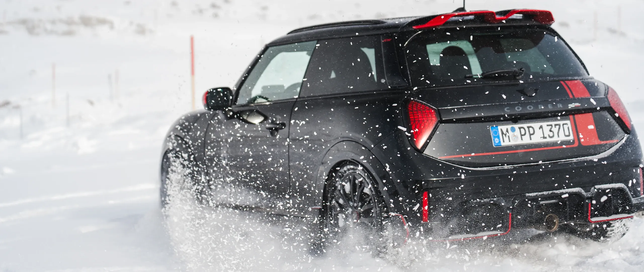 Pohled zezadu na MINI Cooper JCW jedoucí po sněhu.