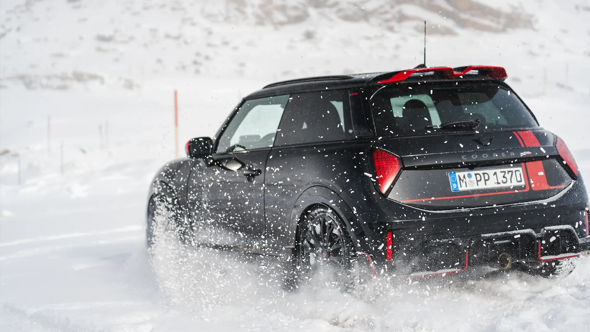 Pohled zezadu na MINI Cooper JCW jedoucí po sněhu.