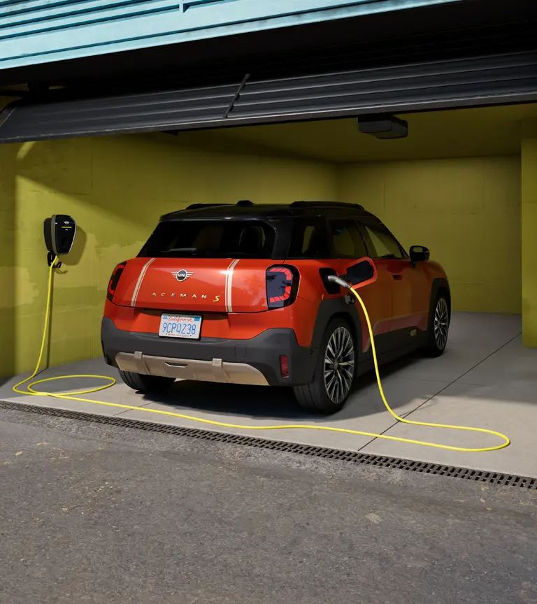 Čistě elektrické MINI Aceman S nabíjené pomocí nabíječky MINI Wallbox Plus, pohled zezadu, zaparkované v garáži.