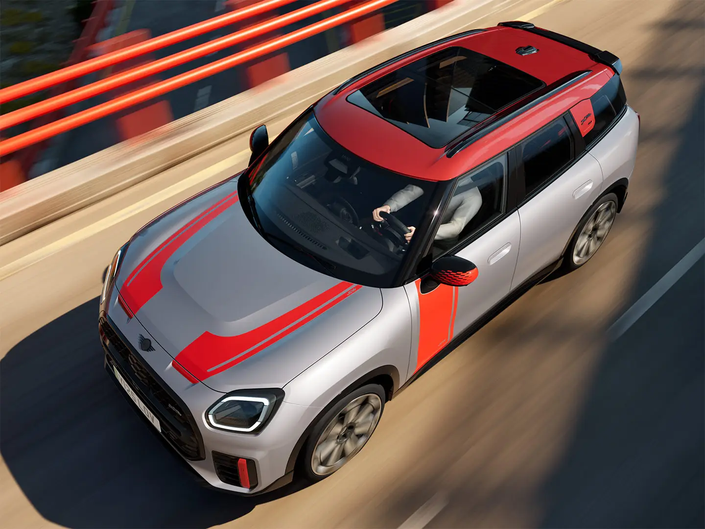 MINI Countryman John Cooper Works ve stříbrné barvě Melting Silver s kryty zpětných zrcátek, polepy na kapotě, střešním spoilerem a wingletem v červené barvě Chili Red – tříčtvrteční pohled zepředu.
