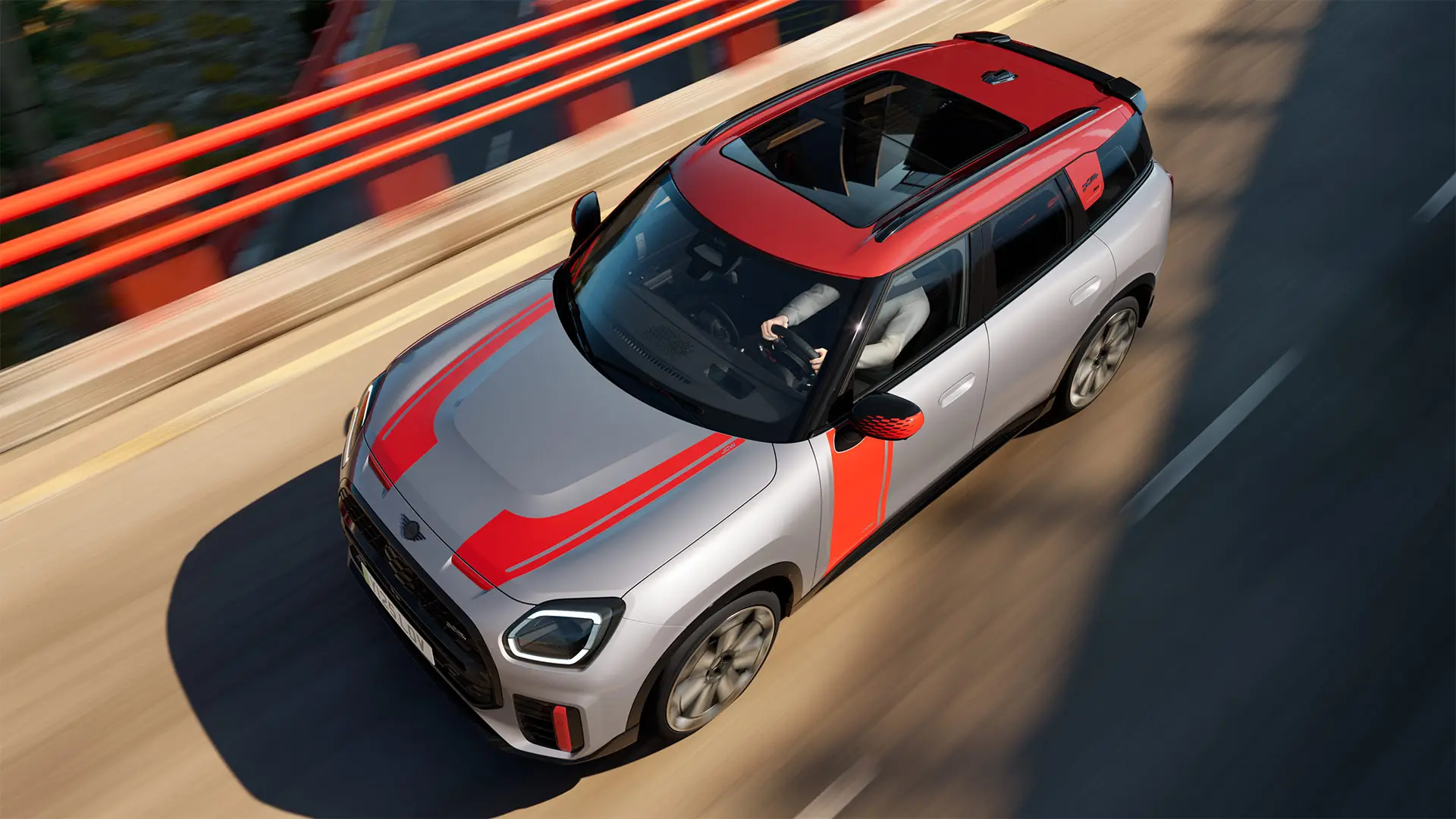 MINI Countryman John Cooper Works ve stříbrné barvě Melting Silver s kryty zpětných zrcátek, polepy na kapotě, střešním spoilerem a wingletem v červené barvě Chili Red – tříčtvrteční pohled zepředu.