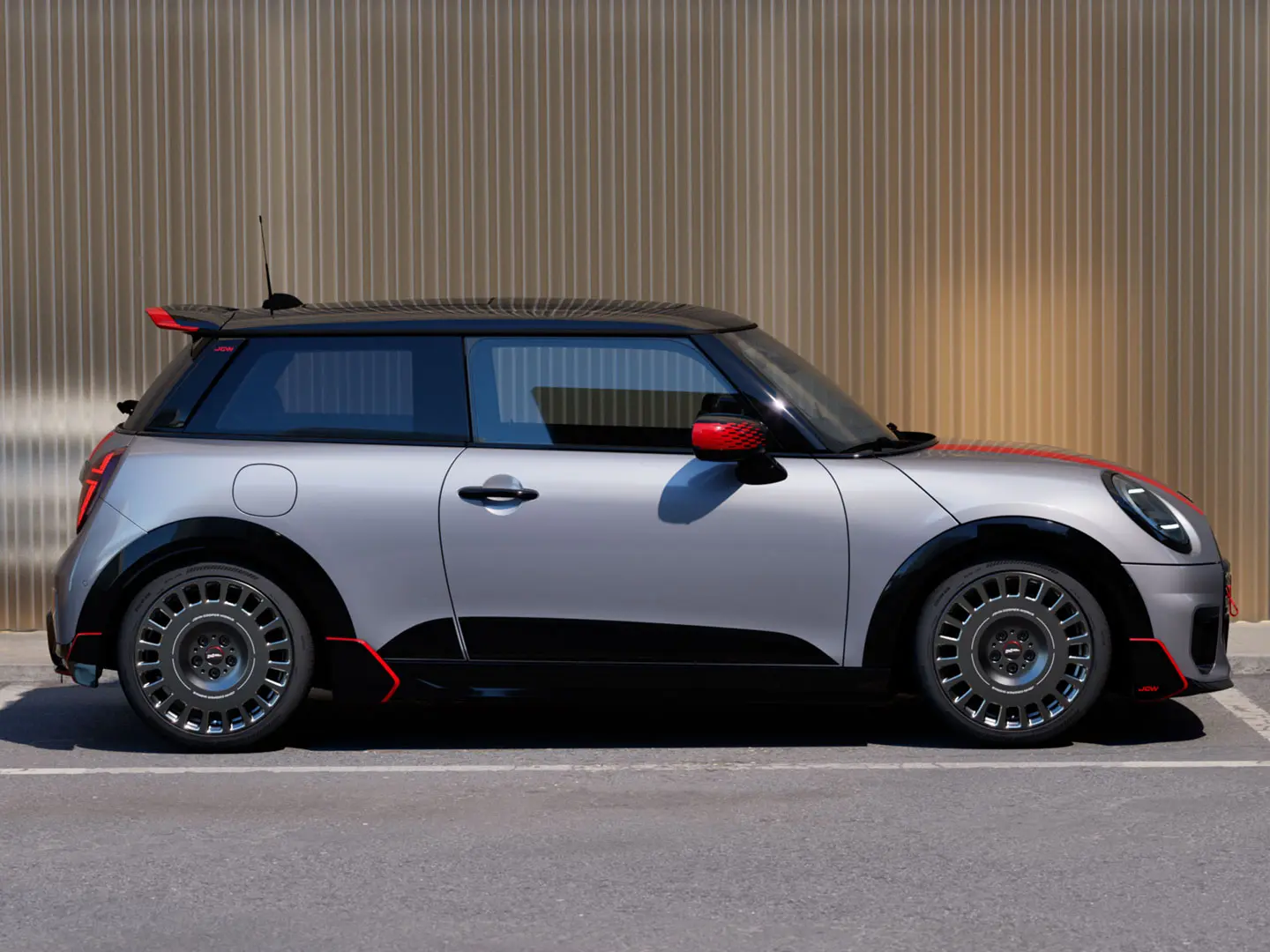 3dveřové MINI Cooper ve stříbrné barvě Melting Silver s John Cooper Works střešním spoilerem vylepšujícím aerodynamické vlastnosti – pohled z boku.