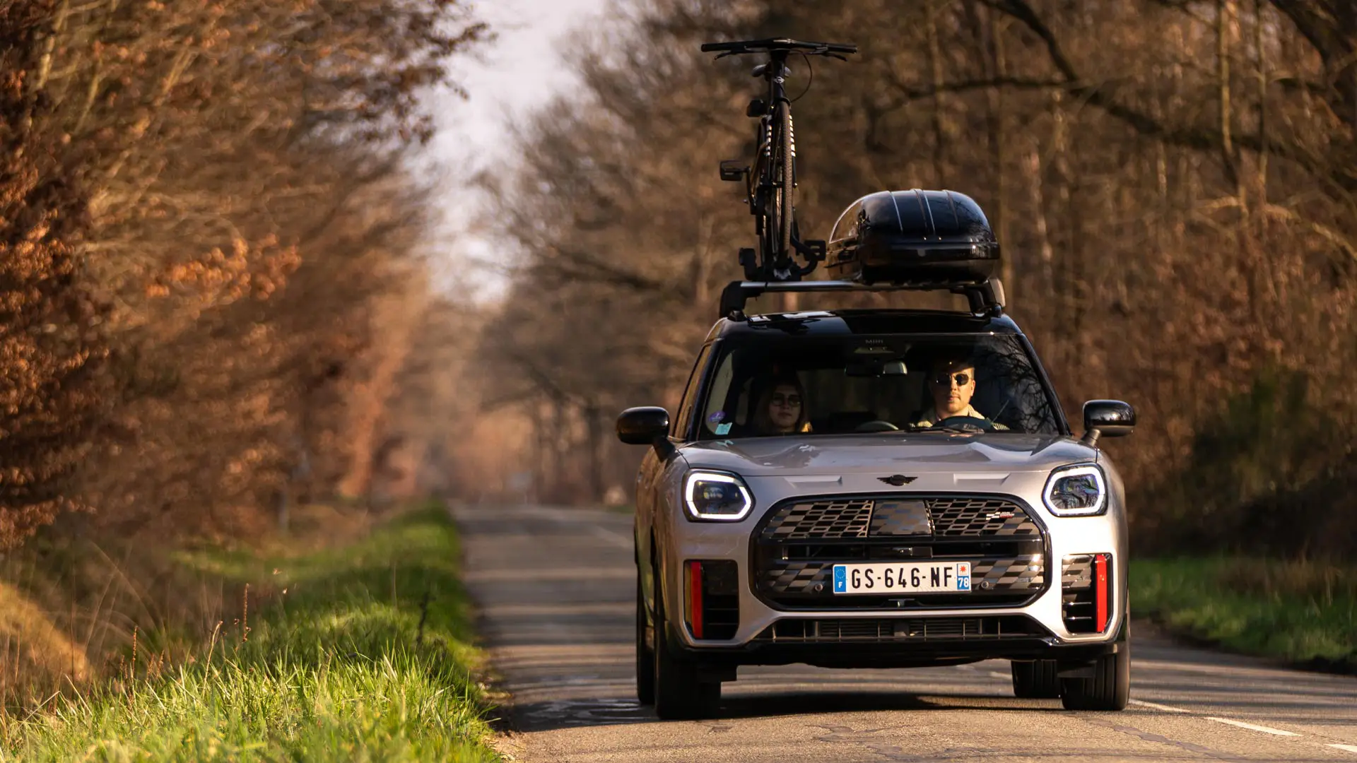 MINI Countryman se střešním boxem na silnici.