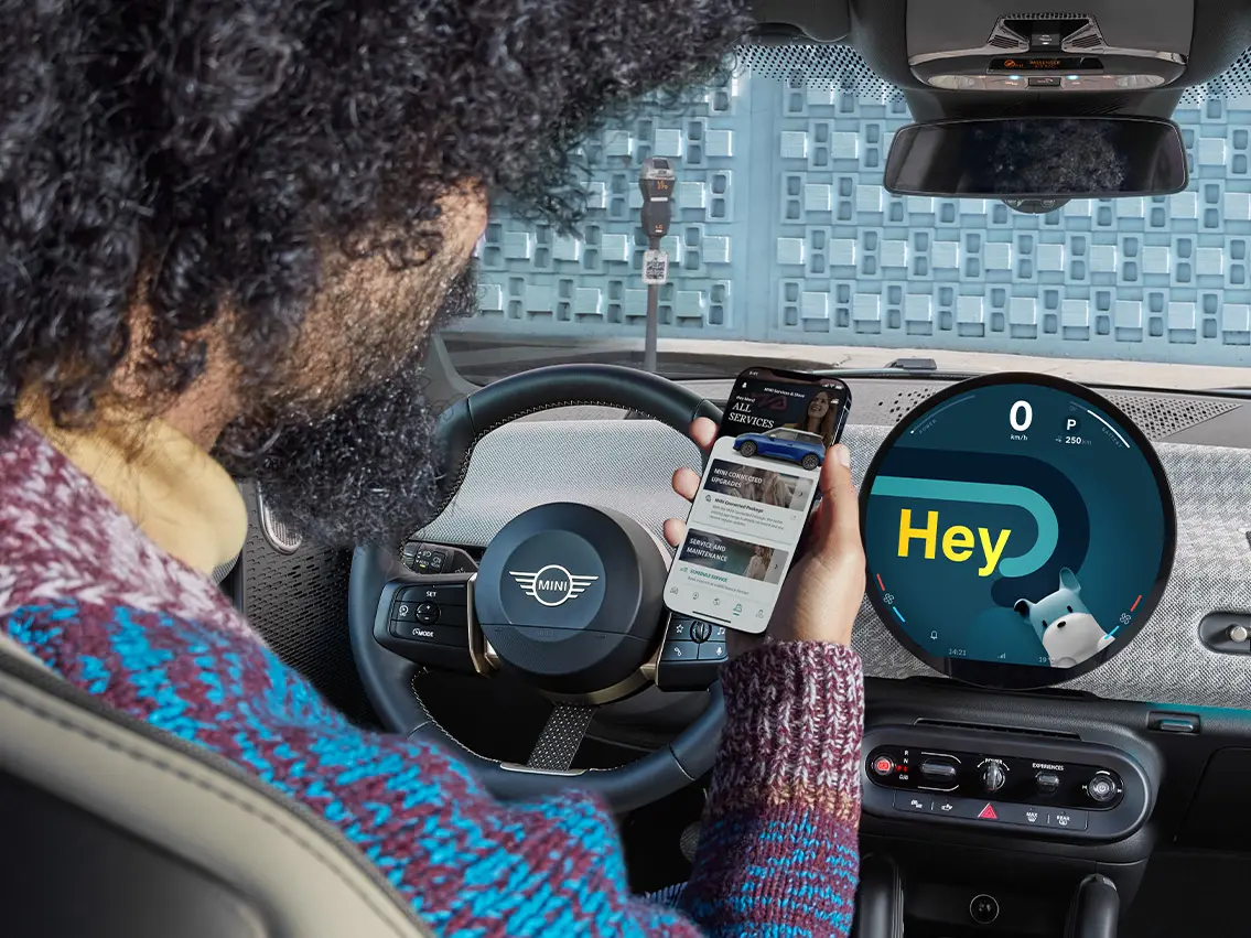 Muž sedící v MINI a dívající se na svůj telefon.
